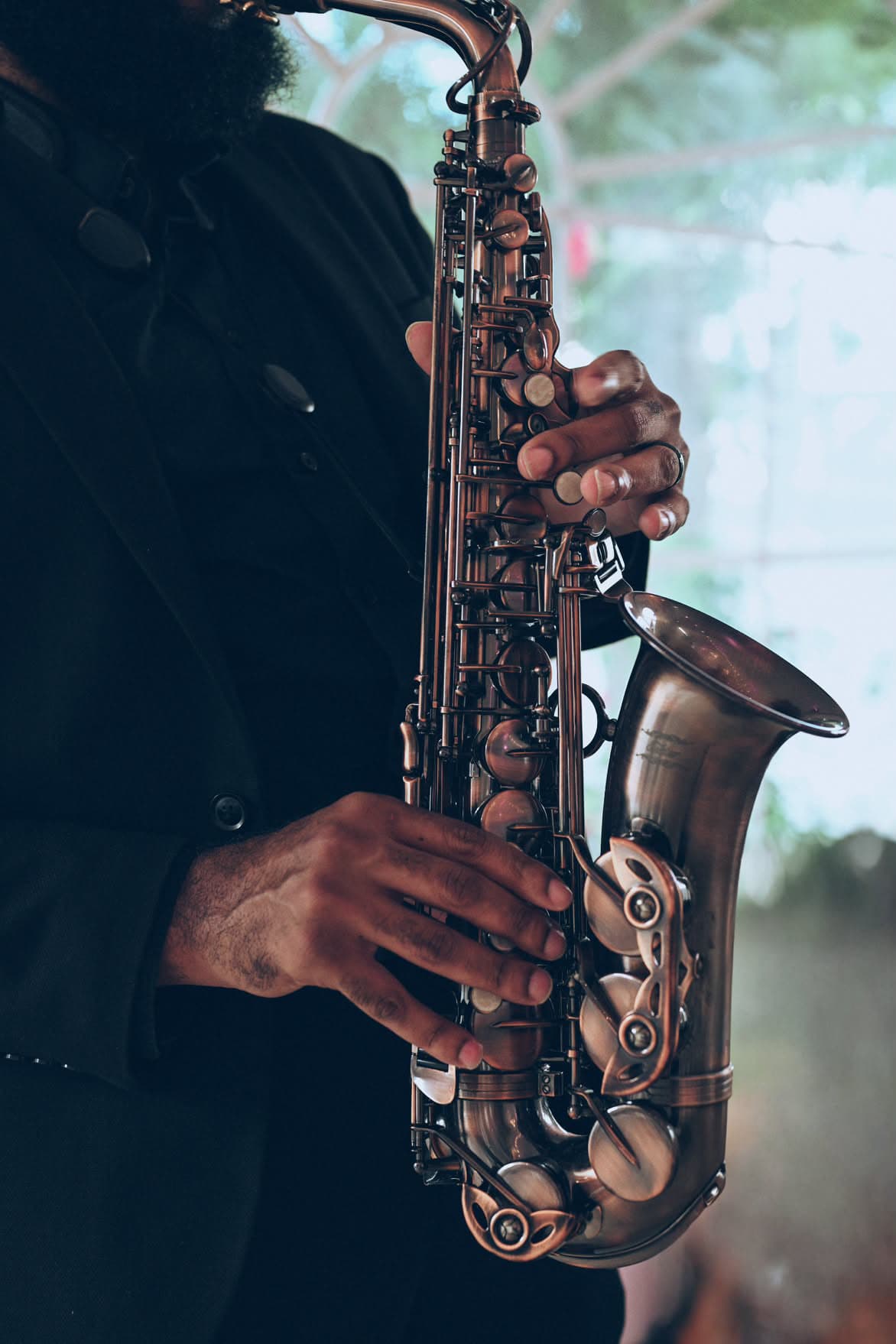 Man in a black suit playing a bronze saxophone with detailed metal keys.