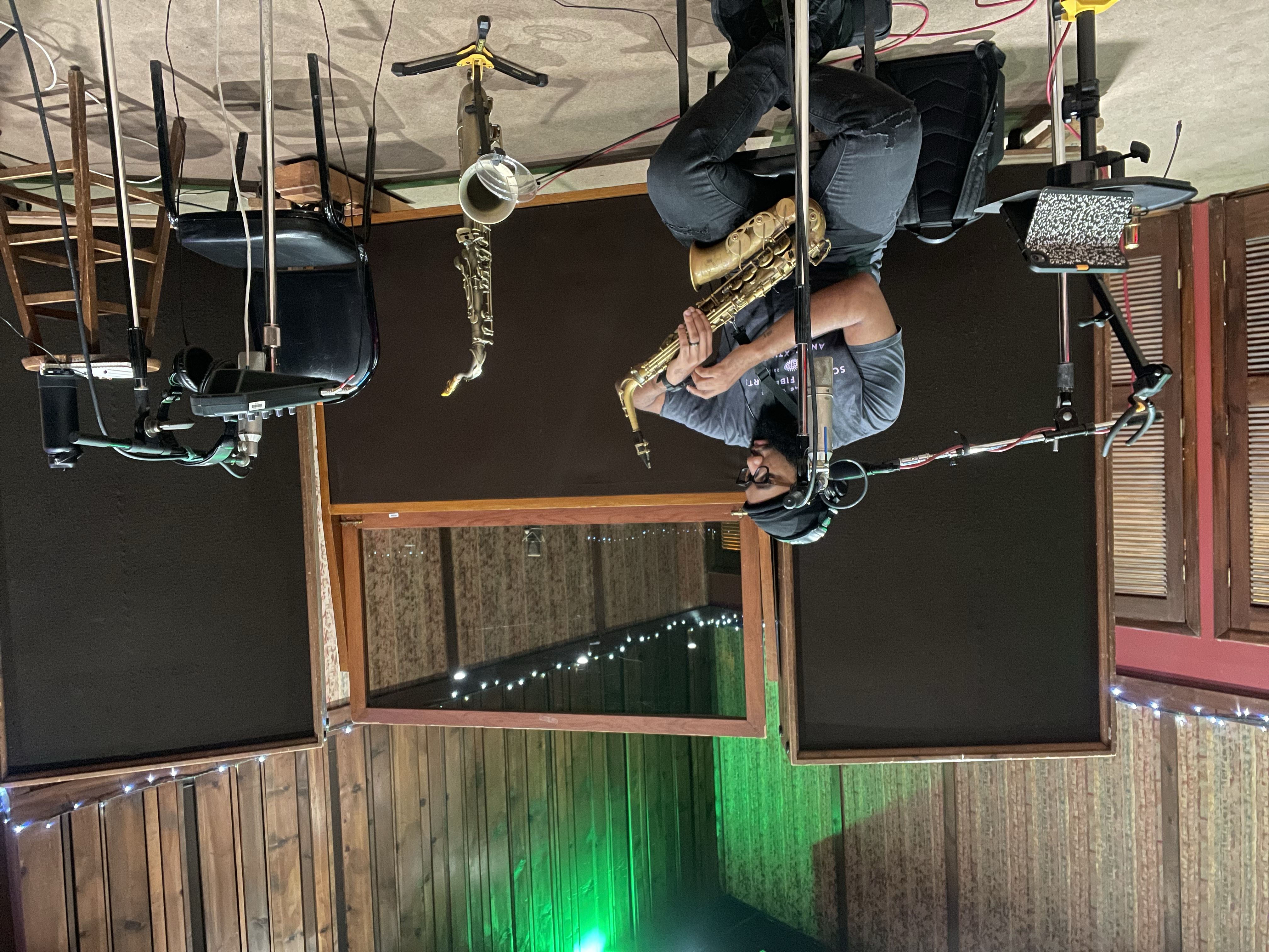 A musician with headphones holds a saxophone in a recording studio while checking his watch.